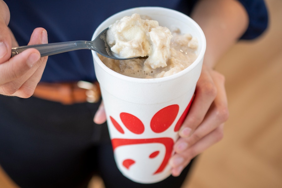 A person using a spoon to scoop ice cream from a root beer float in a Chick-fil-a cup.