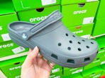 hand holding a Crocs clog in front of shoe boxes