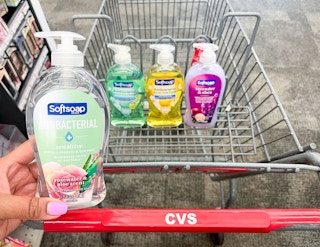 hand holding bottle of Softsoap hand soap in front of shopping cart