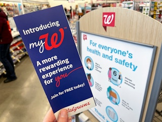A person's hand holding a mywalgreens rewards pamphlet in front of a Walgreens sign.