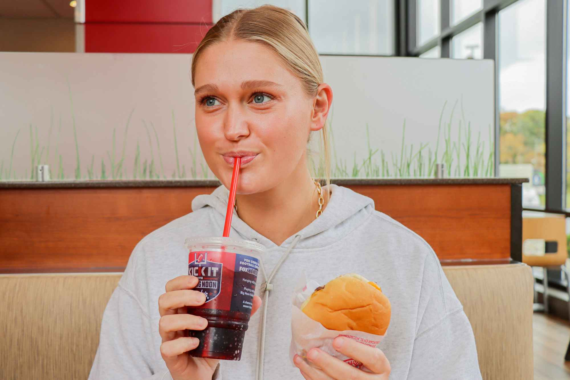 a person taking a drink while holding up a cheeseburger at wendys