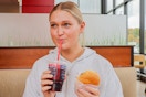 a person taking a drink while holding up a cheeseburger at wendys