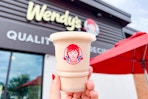 someone holding a frosty outside of a wendys