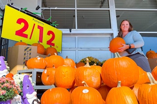 A woman holding a pumpkin in front of the kroger pumpkin display