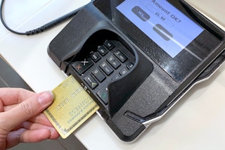 person inserting credit card into point of sale terminal at store checkout