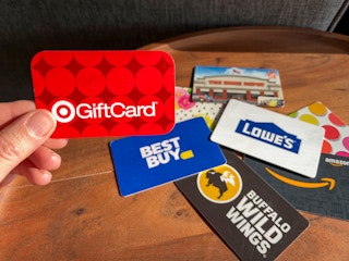 A person holding a target gift card with a bunch of other gift cards on the table behind it.
