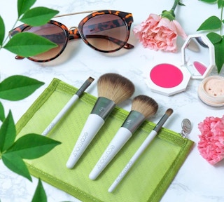 four makeup brushes on a green case with makeup and sunglasses