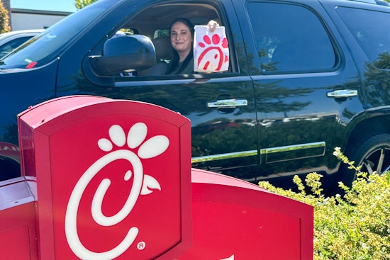 a woamn in a car holding out a chick fil a bag