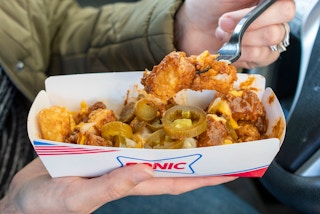 A person scooping a bite full of Sonic loaded tots from a cardboard fast food dish.