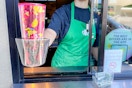 a starbucks working holding out a personal cup out a window 