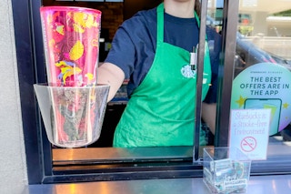 a starbucks working holding out a personal cup out a window 