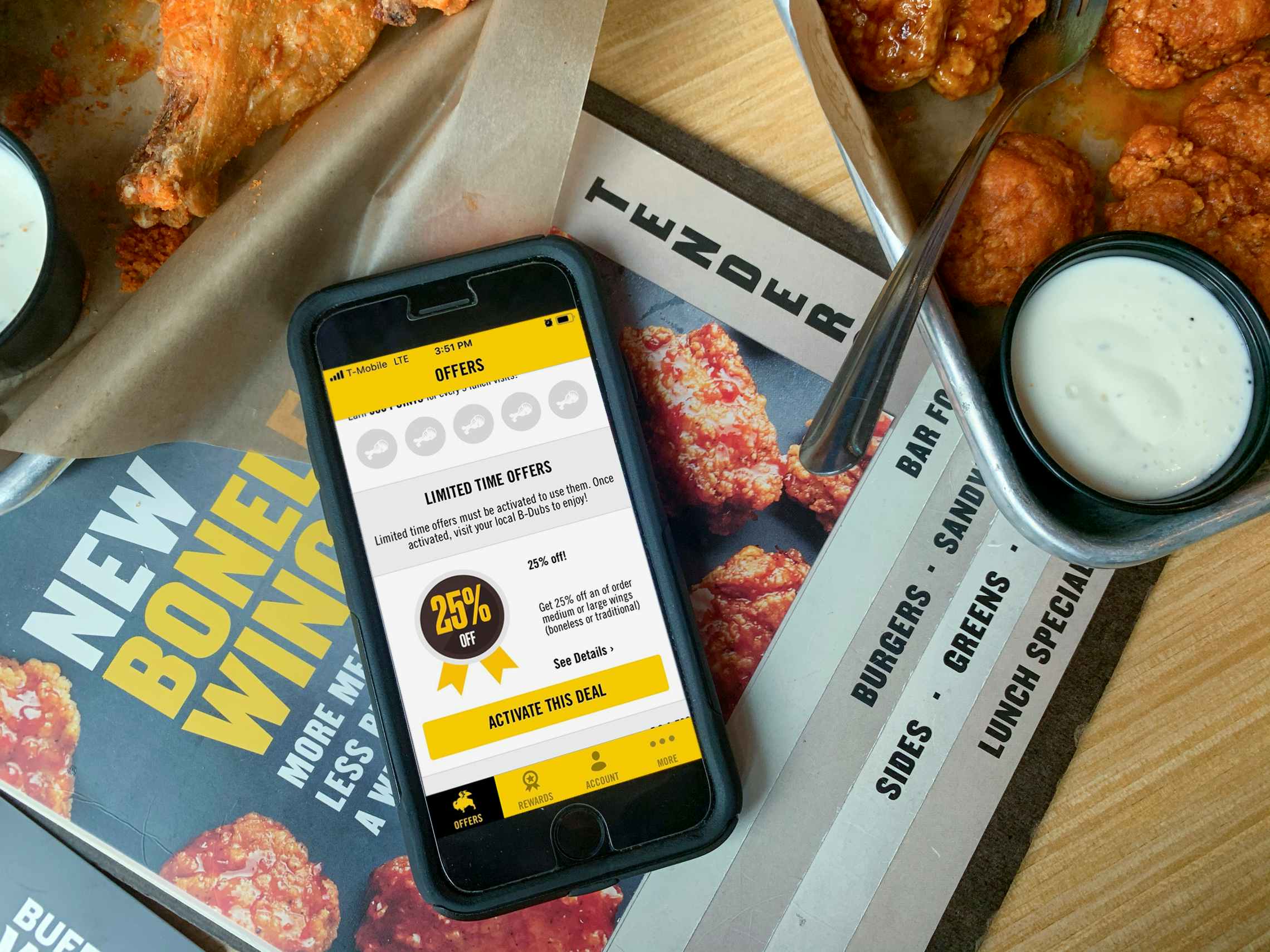 An iPhone sitting on top of a menu on a table, open to the Buffalo Wild Wings app's Offer page. The page shows a 25% off deal that can be...