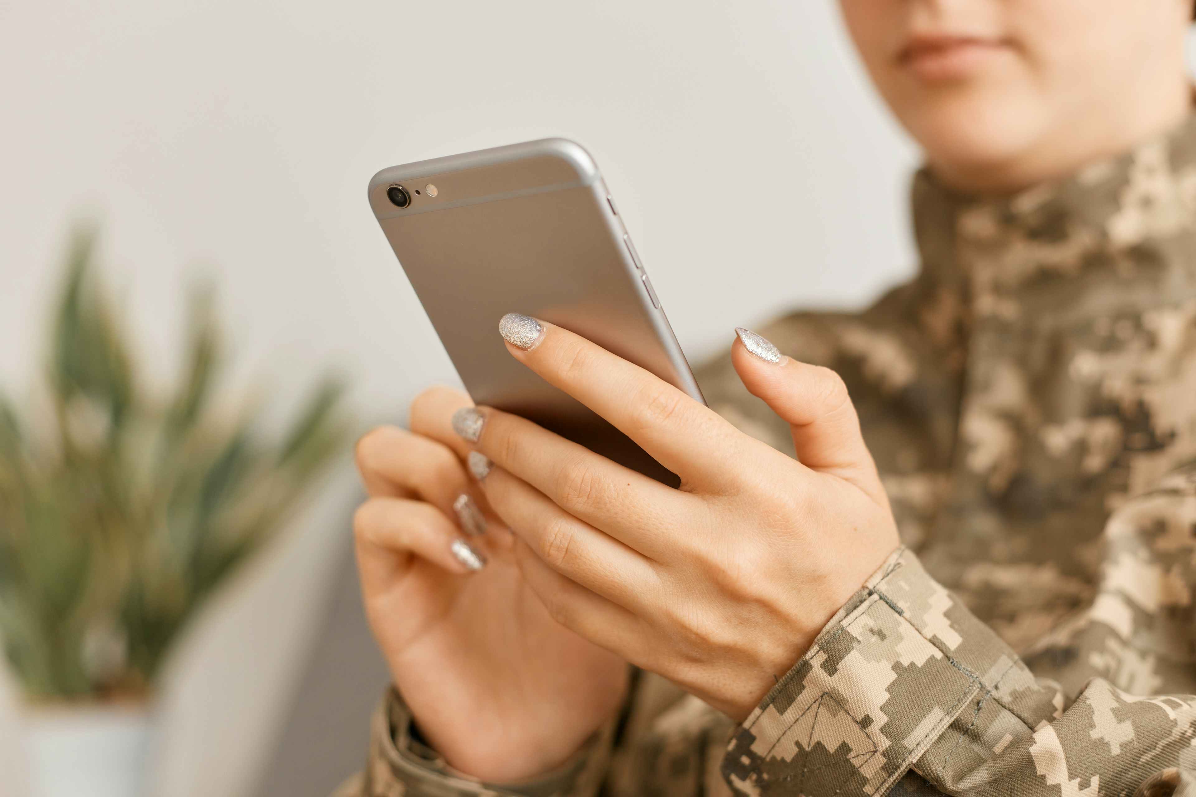 A woman wearing a military uniform, looking at a cell phone.