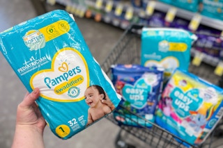 hand holding pampers diapers with a walgreens cart filled with more packs of pampers diapers and easy ups