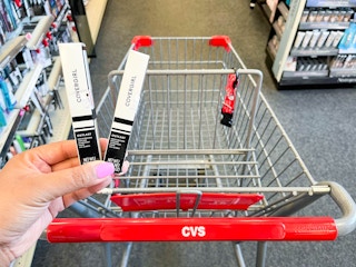 hand holding two Covergirl lipcolor products in front of CVS shopping cart