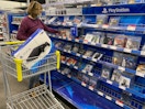 A person shopping for PlayStation games in Best Buy with a PS4 in the cart.