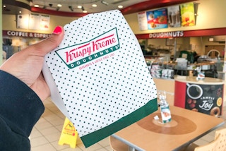 a person holding up a Krispy Kreme bag.