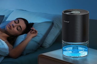 A woman sleeps next to a dehumidifier on a side table in a dark room.