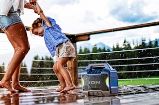Lifestyle image of adult and child dancing in the rain to the Ion portable speaker