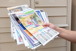 woman holding a bunch of newspaper inserts near a community mailbox area