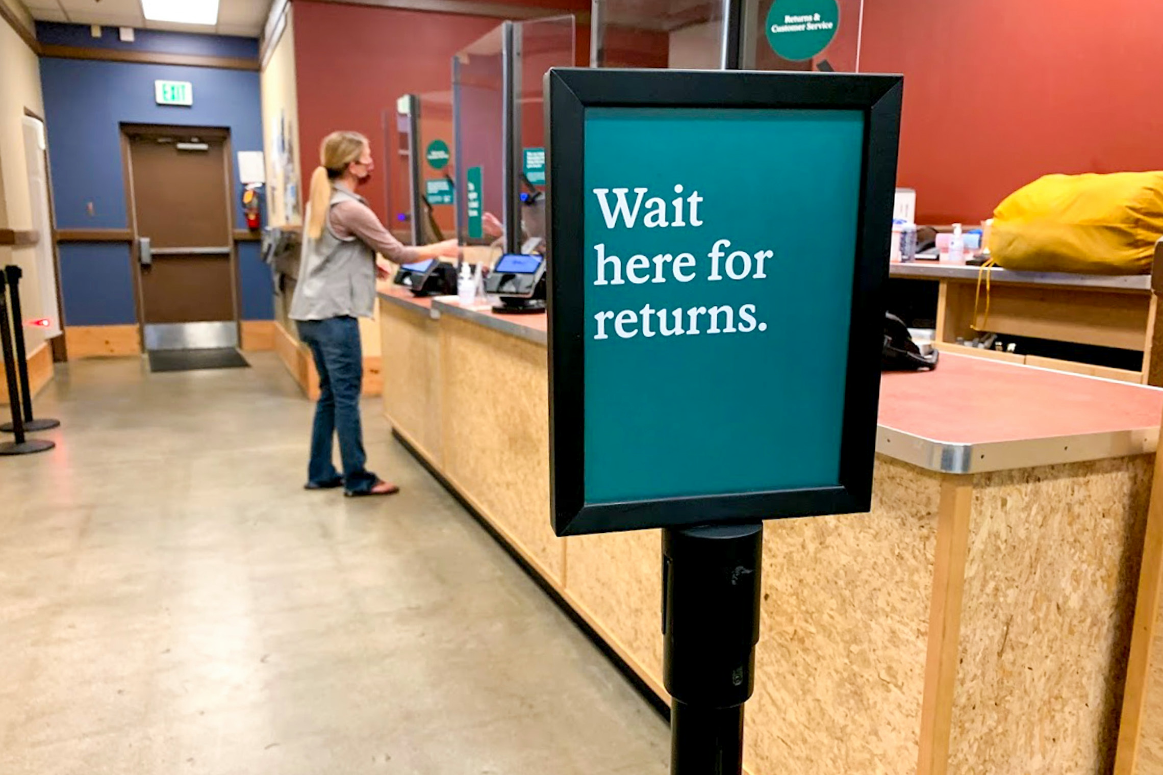 A person standing at the return counter with a "Wait here for returns" sign inside REI.