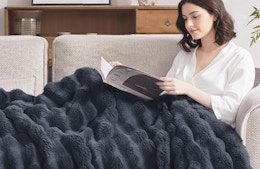 a person laying with a grey faux fur blanket