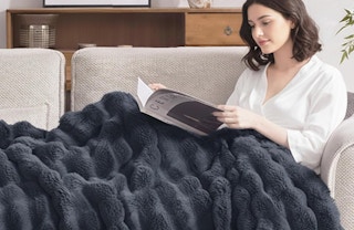a person laying with a grey faux fur blanket