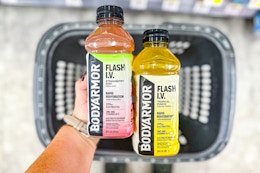 person holding 2 body armor drinks over a basket