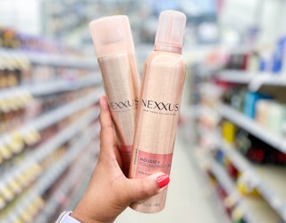 Hand holding a can of Nexxus Voluminizing Foam and a can of Nexxus Finishing Mist in aisle