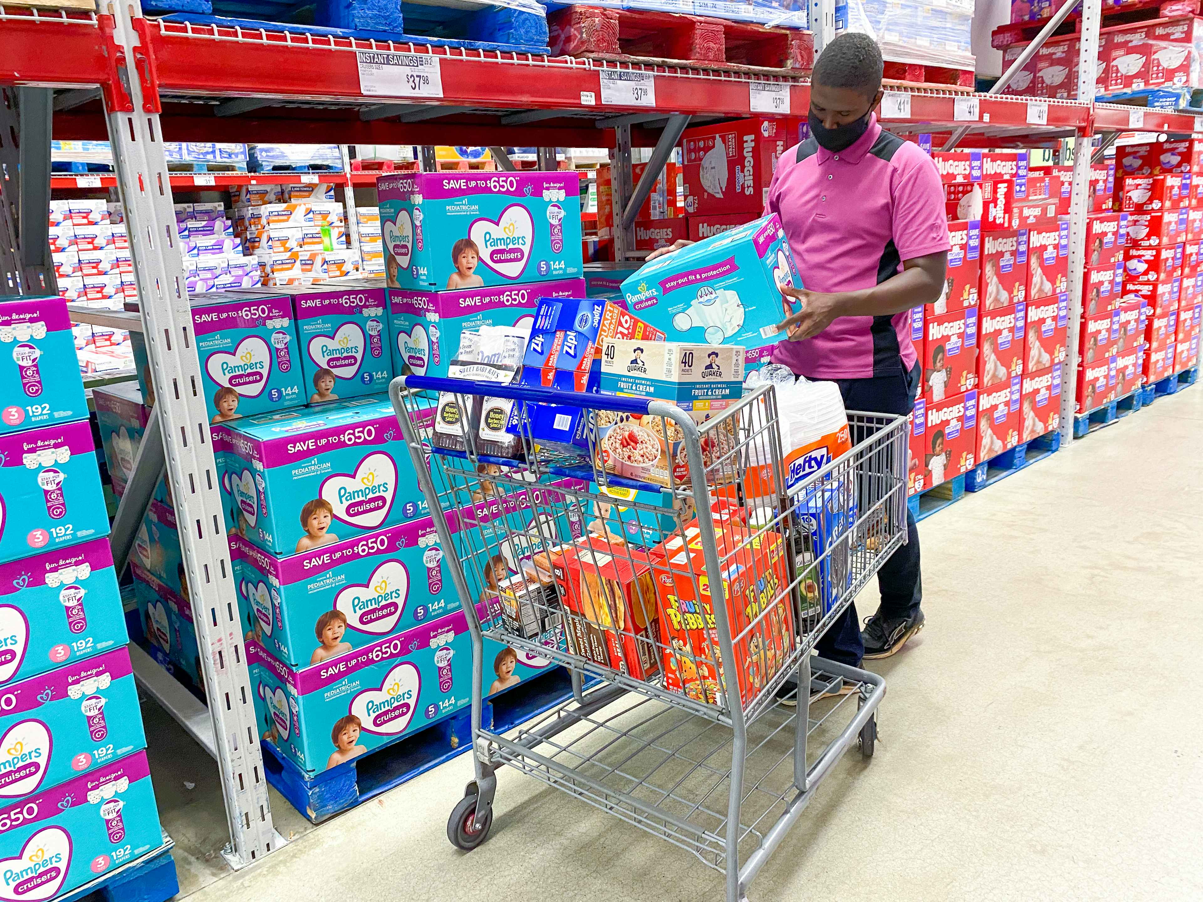 A man in the diaper aisle at Sam's Club putting a box of Pampers diapers into his shopping cart.