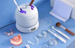 a retainer cleaner on a blue table with dentures, retainers, and toothbrushes