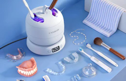 a retainer cleaner on a blue table with dentures, retainers, and toothbrushes