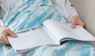 someone on the couch reading a book with a blue and white marble blanket