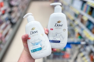 hand holding two bottles of dove hand soap in front of shopping cart in store aisle