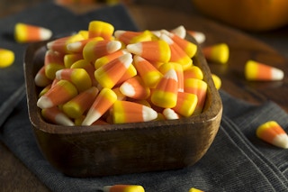 A wooden bowl of candy corn sitting on a table.
