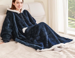 a person laying on a bed with a wearable blanket hoodie