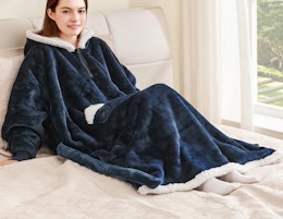 a person laying on a bed with a wearable blanket hoodie