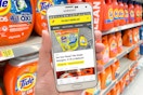 Krazy coupon lady app displaying a deal on laundry detergent, in front of Tide on the shelves of the detergent aisle inside Walmart.