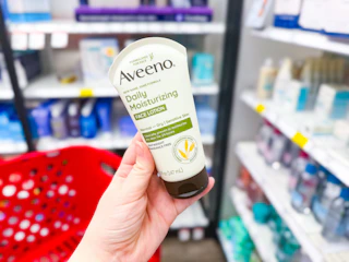 hand holding a bottle of aveeno face lotion in front of a target cart
