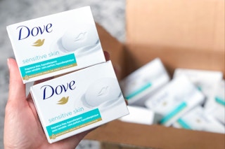 person holding two dove sensitive skin bar soaps near shipping box