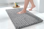 A grey 24 x 17 inch shaggy chenille bath rug is being stepped on.
