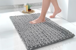 A grey 24 x 17 inch shaggy chenille bath rug is being stepped on.
