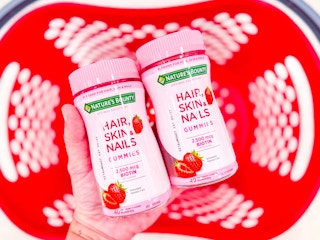 hand holding 2 nature's bounty hair, skin, nails gummies over a target basket