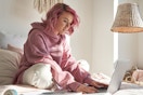 young teenager with pink hair with laptop on bed