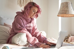 young teenager with pink hair with laptop on bed