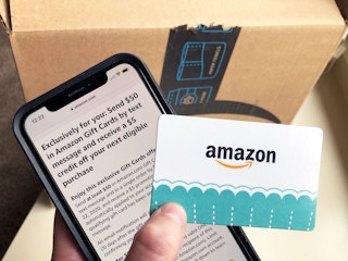 An amazon gift card held next a cell phone and amazon box