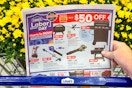 a person holding a lowe's labor day sales ad in store in front of a lowes cart full of mums 