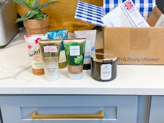 body lotions and a three-wick candle on a countertop next to a Bath & Body Works shipping box