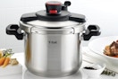 A stainless steel T-Fal Clipso Pressure cooker sits on a counter between a cutting board and a plate of food. It has secure-locking 1-handed