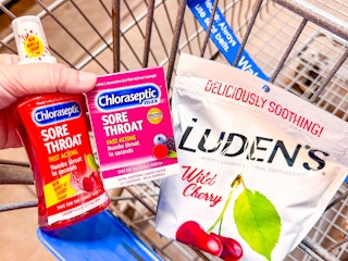 hand holding chloraseptic throat spray and lozenges with ludens drops in walmart cart